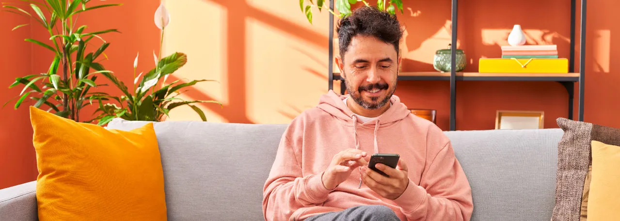 Pessoa sentada ao sofá sorrindo e rolando a tela do celular