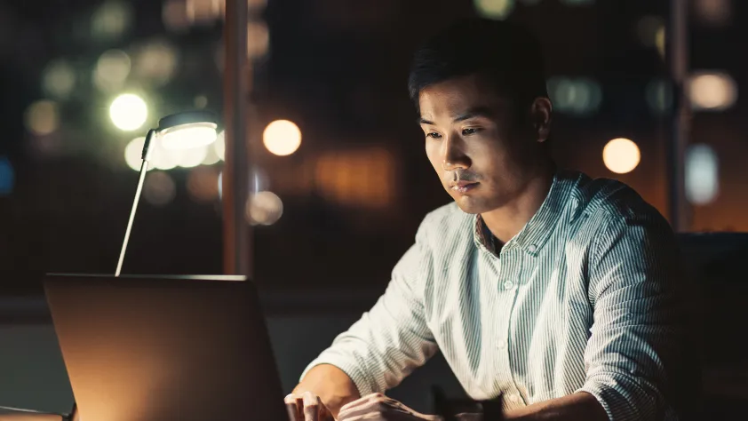 Person sitting at desk working on laptop in the evening