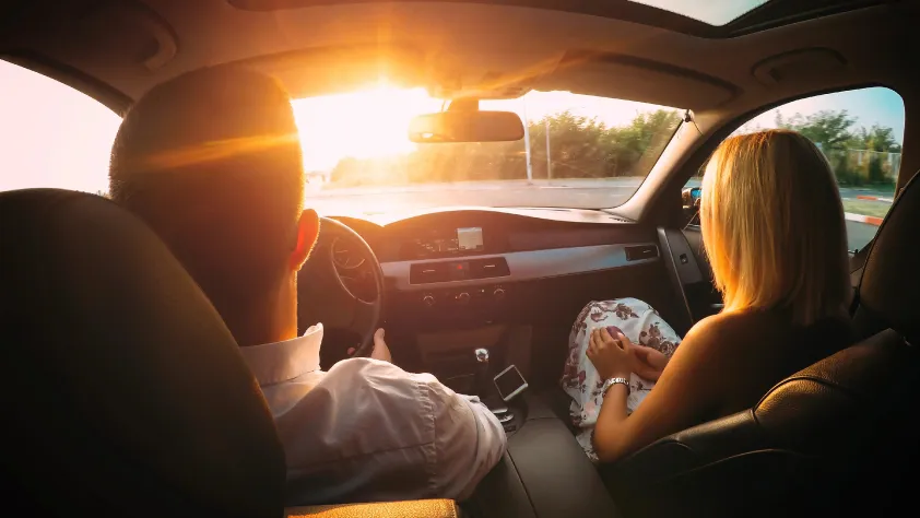 Dos personas conduciendo un auto al atardecer