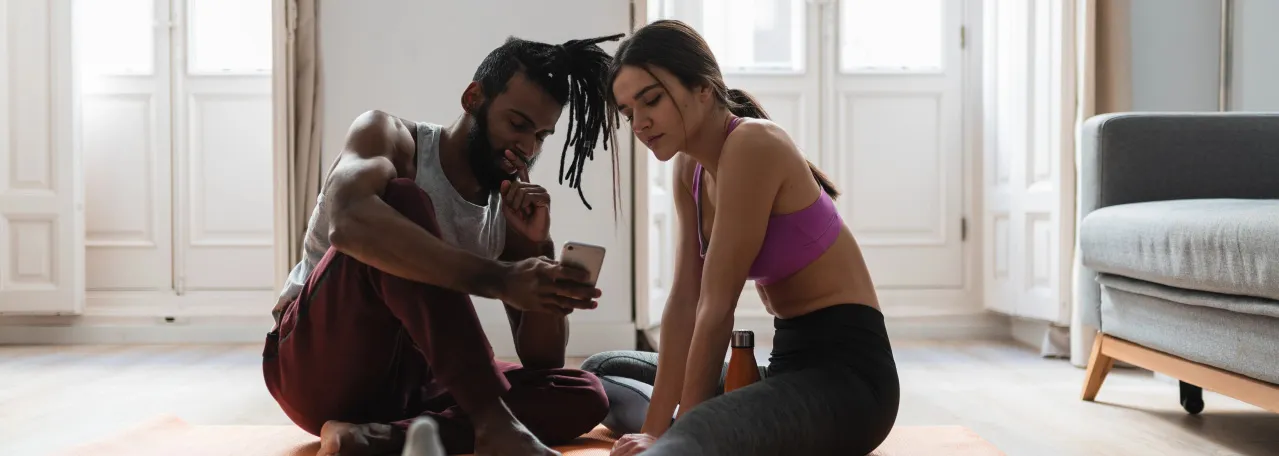 Duas pessoas sentadas no chão após a aula de ioga lendo uma notificação do WhatsApp