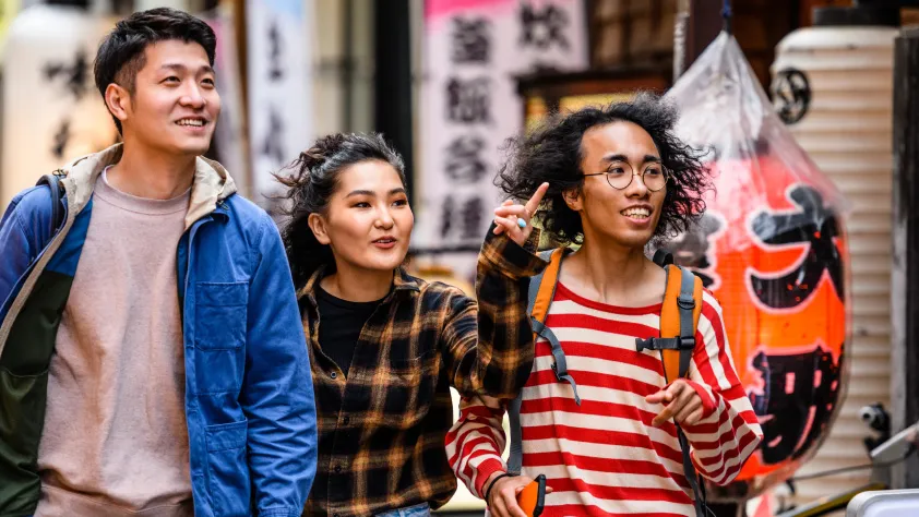 Three people walking by Asian storefront