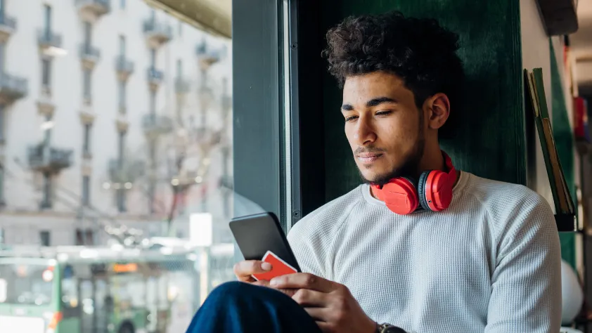 Persona sentada contra una ventana leyendo un mensaje de WhatsApp del banco