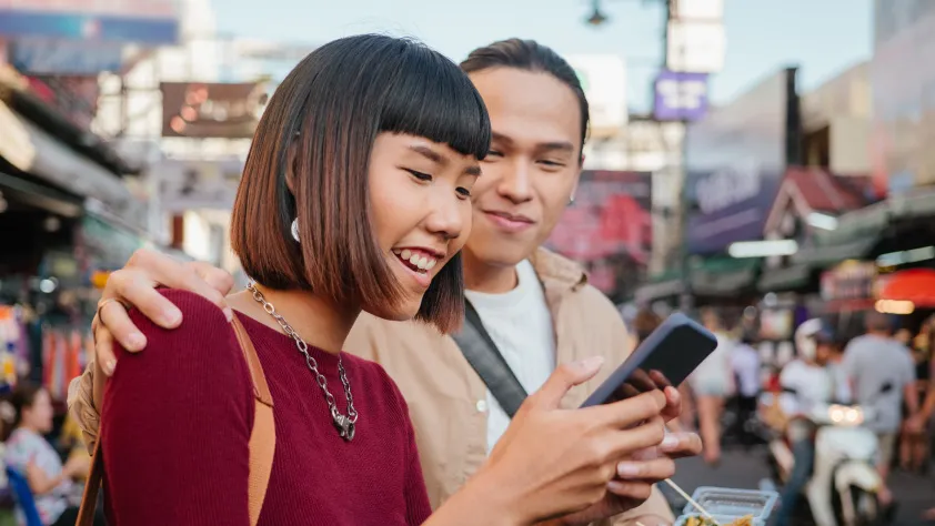 Duas pessoas no meio de um mercado de rua sorrindo para o celular