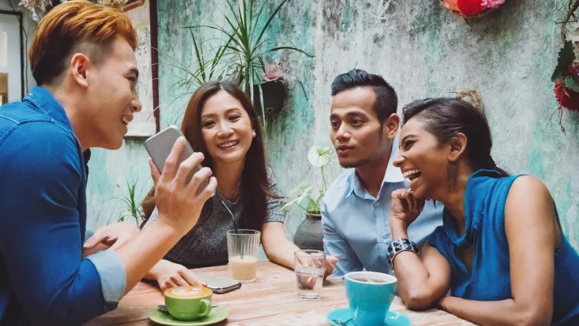 Four people gathered around table at cafe while one person shows something on their phone