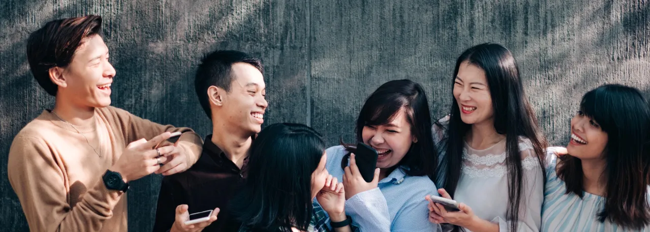 Group of six people laughing and holding their phones