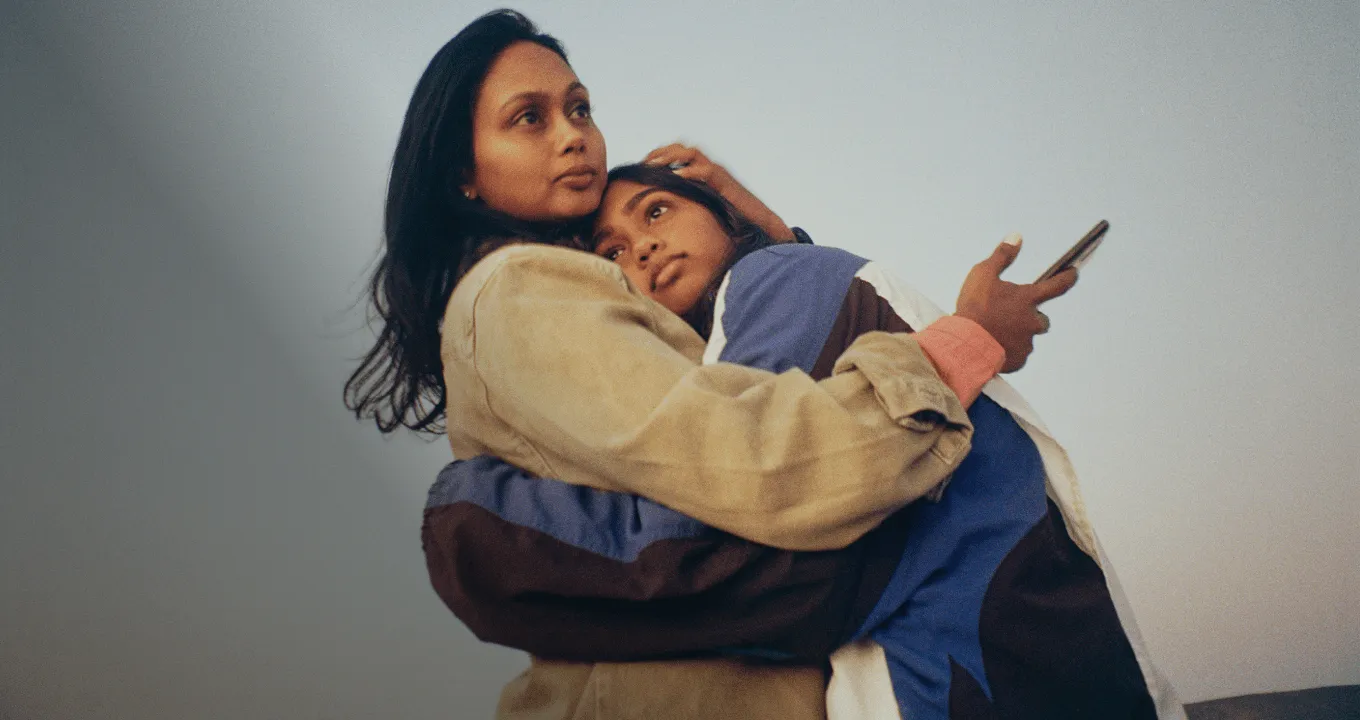 mother and daughter hugging while holding mobile device