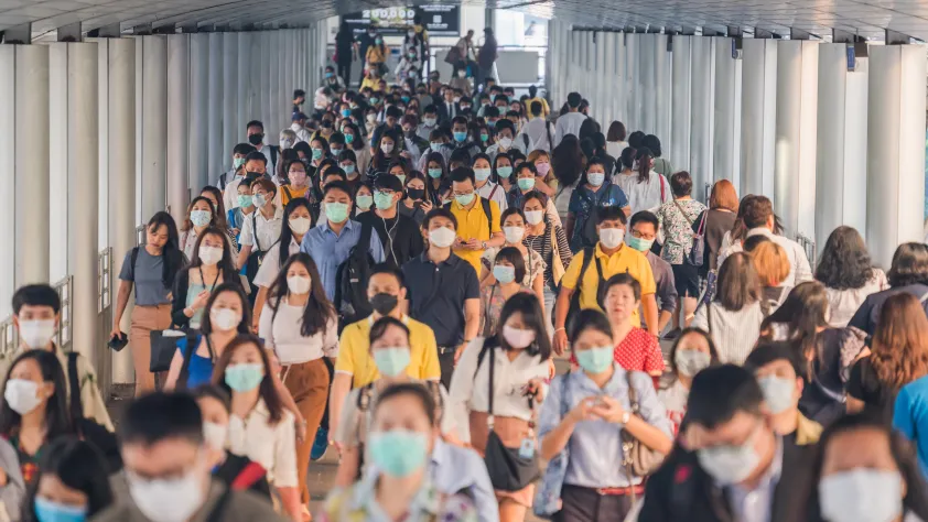 Large group of people wearing masks walking out of a public transportation station
