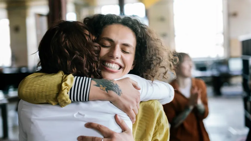 One person smiling while hugging a friend