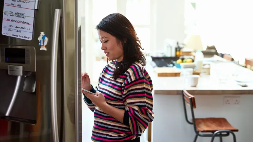 Person standing in front of open refrigerator checking phone