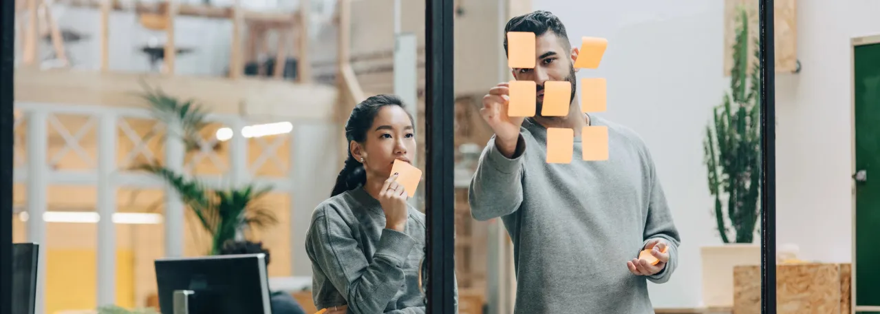 Two colleagues brainstorming using post-it notes on office window
