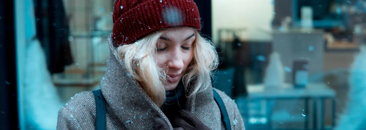 Persona parada en la nieve con los ojos cerrados con un abrigo grande y gorro