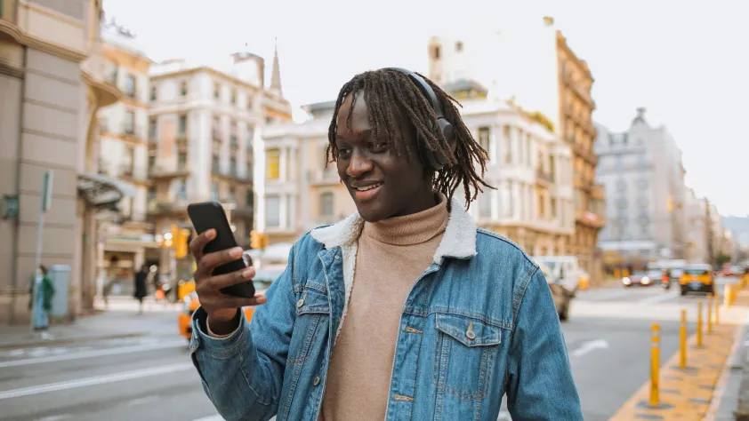 Persona caminando por una calle con auriculares y revisando su teléfono