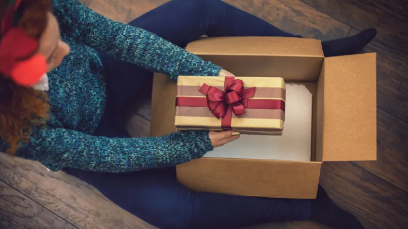 Persona sentada en el piso abriendo un paquete con un regalo