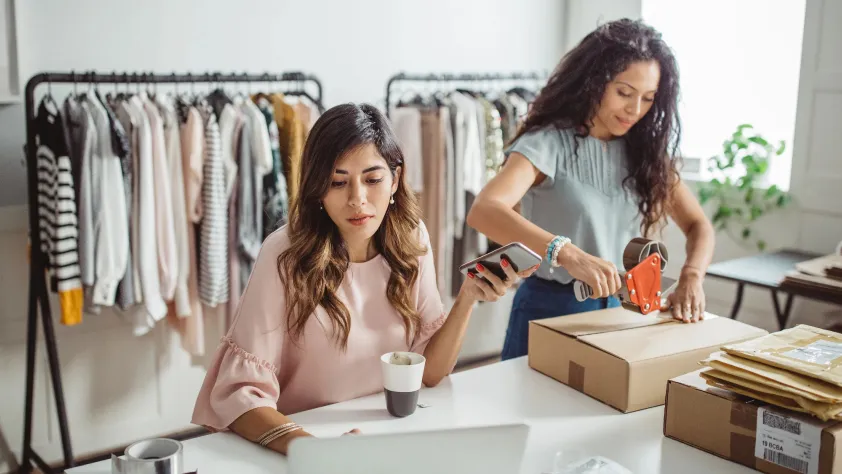 Two people checking orders on laptop and packing clothing orders to send out