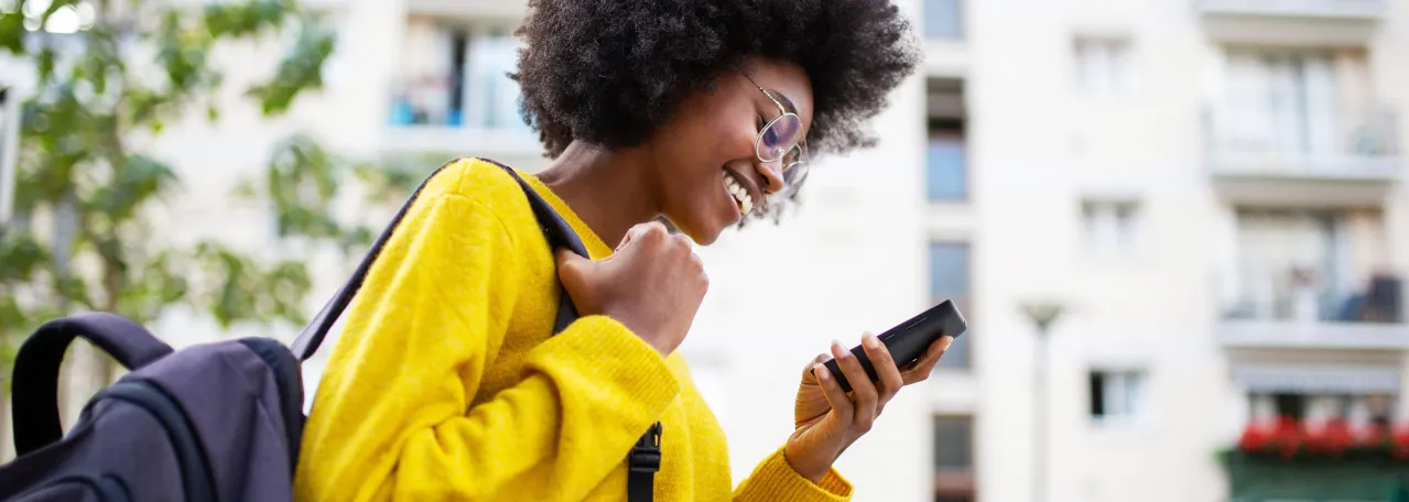 Person walking and carrying backpack while smiling at phone