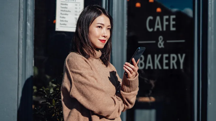 Person standing outside of bakery while holding phone