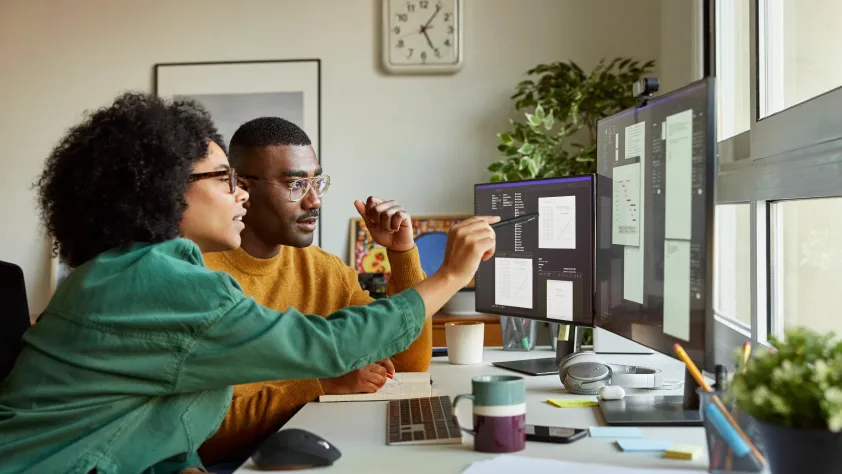Two people sitting at desk while one explains a design example on the computer