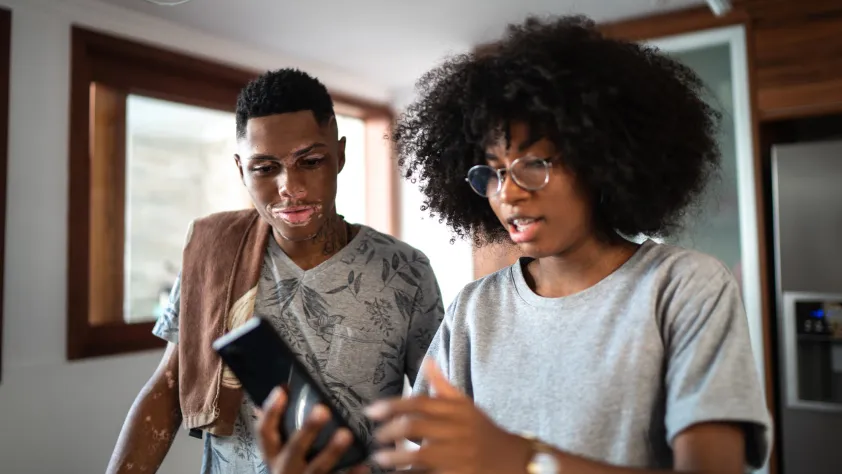 Two people standing in kitchen, both looking at one person's phone