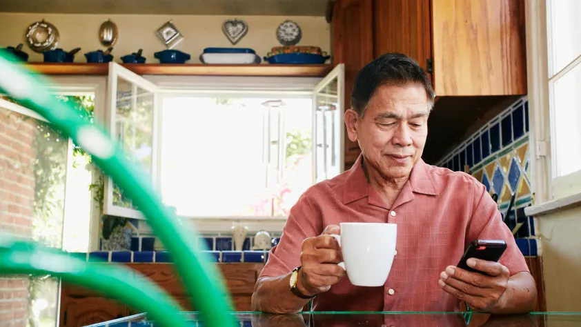 Pessoa bebendo café na cozinha enquanto mexe no celular