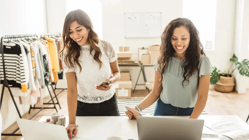 Two people smiling while working on their laptops in their home office