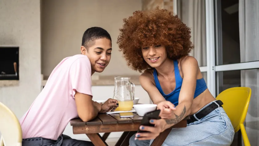 Duas pessoas sentadas à mesa do café da manhã enquanto uma mostra à outra uma compra online pelo WhatsApp