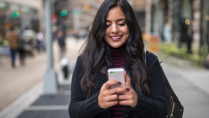 Pessoa andando pela rua lendo uma mensagem empresarial no WhatsApp