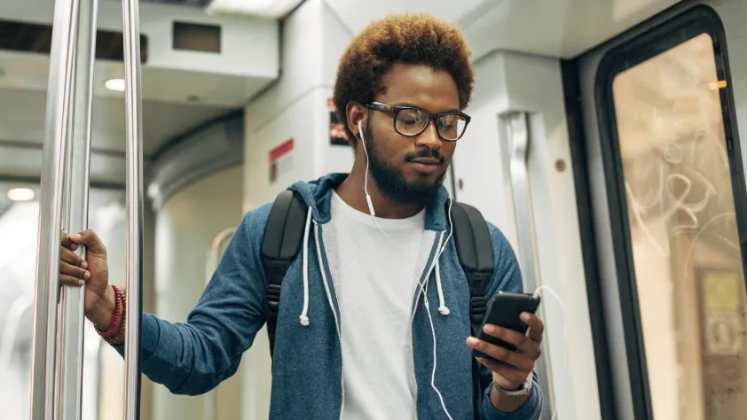 Pessoa em um ônibus, usando fones de ouvido e lendo uma mensagem de texto no celular