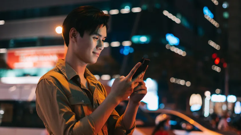 Person standing on sidewalk during the evening in front of lit up building while reading a WhatsApp message
