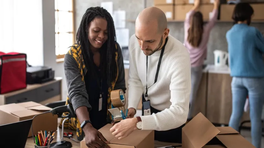 Two people in an office putting together a package to send out