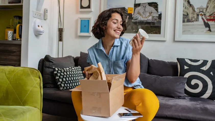 Person sitting on couch while opening a new package containing a ceramic cup