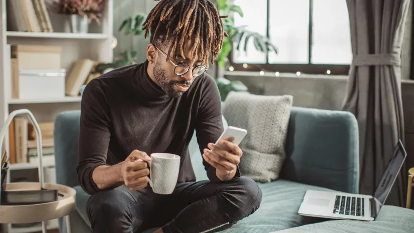 Person sitting on couch drinking coffee while reading a WhatsApp message