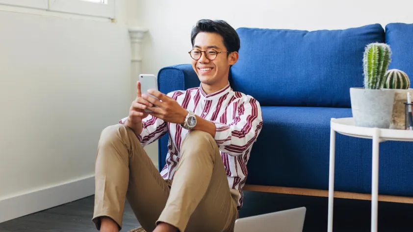 Person sitting on floor against couch, smiling while checking messages on WhatsApp