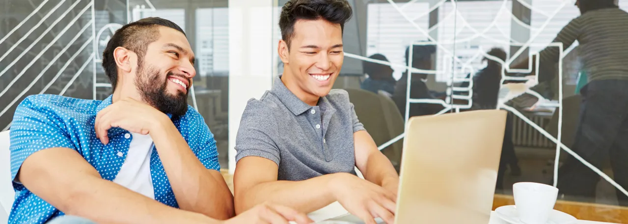 Two people smiling while working on a laptop in a conference room