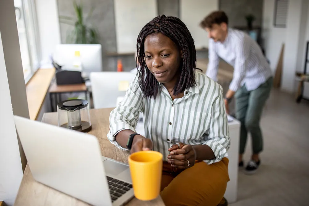 Person holding a mug looking at a laptop