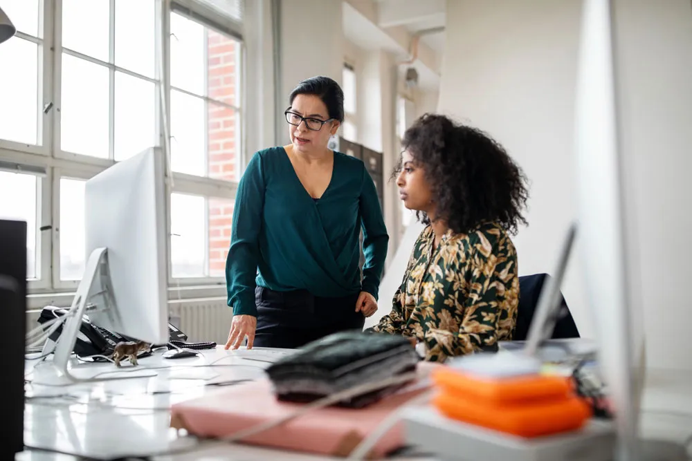 Two women having a discussion while looking at the desktop computer in an office