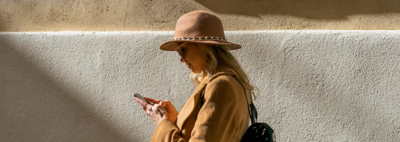 Person walking in front of beige wall while reading a WhatsApp message on phone