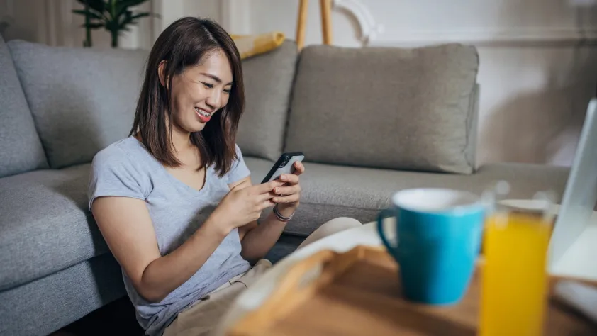 Person sitting on floor against the couch, while smiling and making a jean order via WhatsApp
