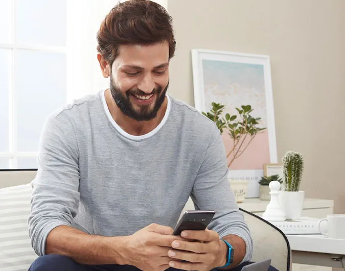 Un homme regardant un téléphone en souriant assis sur un canapé