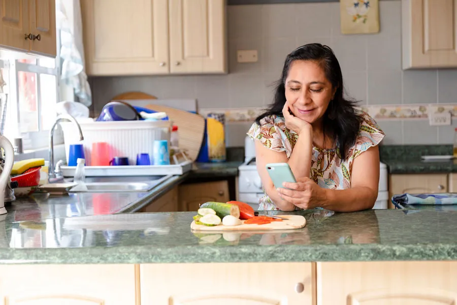 Una mujer que revisa su teléfono en la mesada de la cocina.