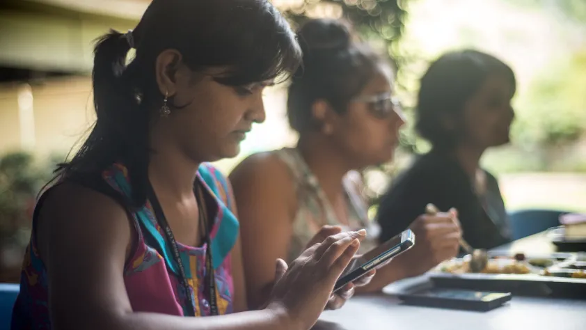 Three people sitting at lunch table while chatting and looking at Facebook ad on phone