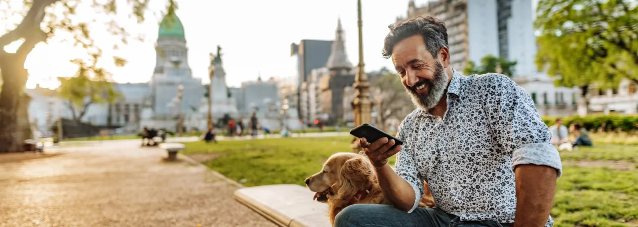 Person sitting with dog in city center while smiling and looking at phone