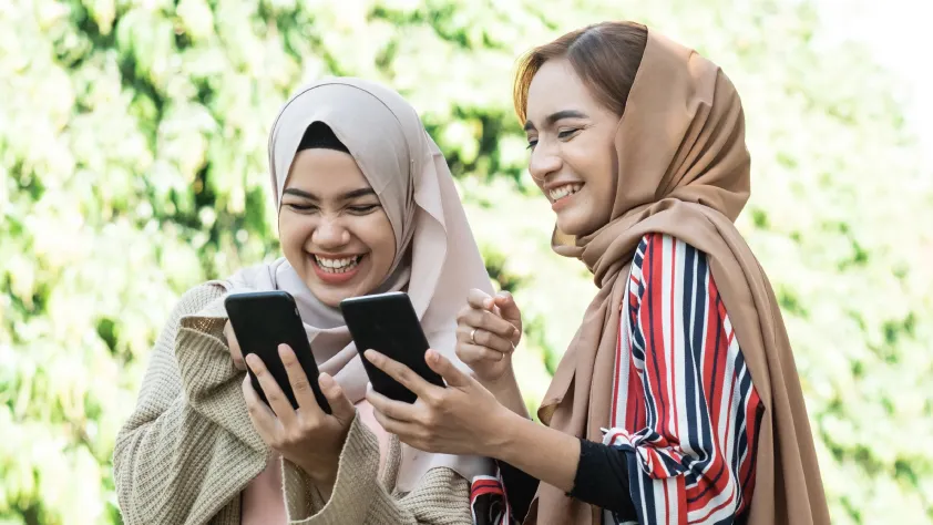 Two people laughing while showing each other ads on their phones