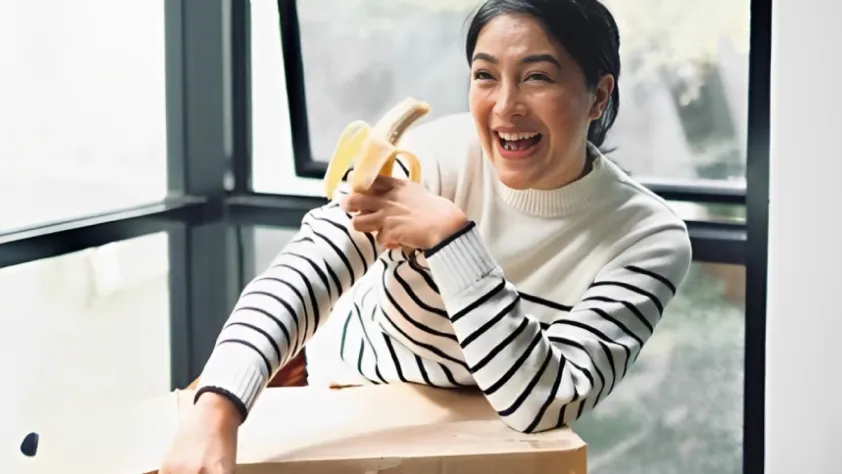 Person sitting at desk holding a banana and laughing