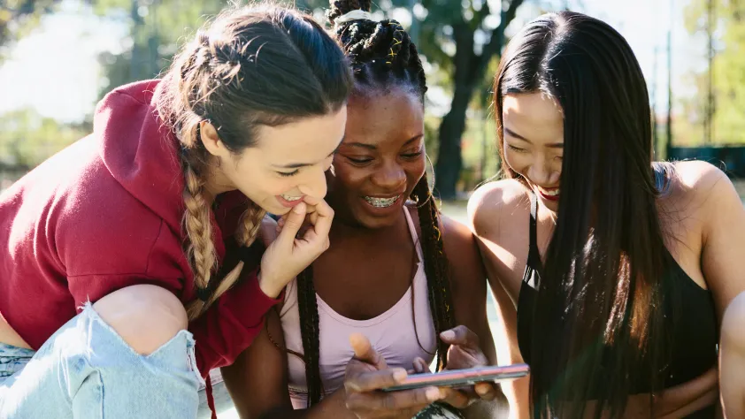 Three teens sitting and laughing together while watching a video on their phone