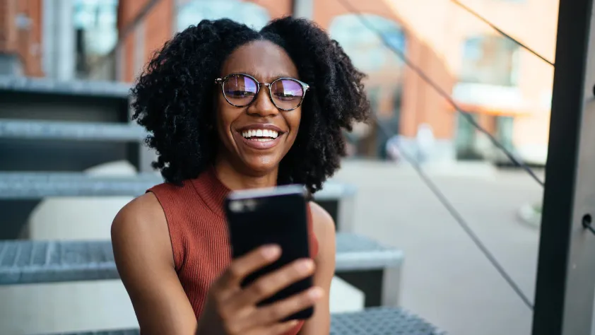 Person sitting on stairs outside while smiling at phone