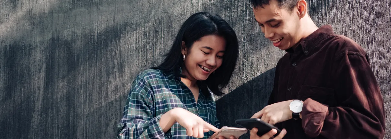 Two people standing in front of wall showing each other ads by pointing at their phones