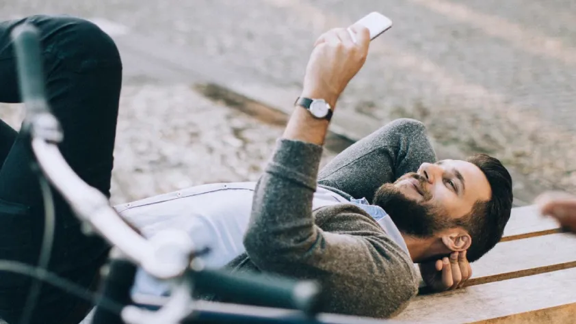 Person laying on outdoor bench while smiling and reading a marketing message on phone through WhatsApp