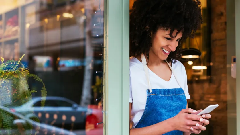 Small business owner standing in storefront while smiling and looking at phone