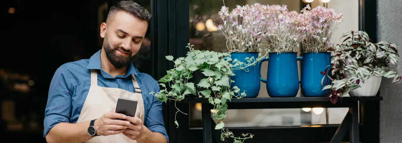 Florist owner standing outside store while replying to a customer message via WhatsApp