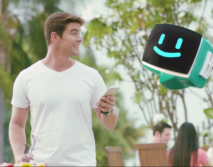 A man gazing at a suspended, smiling robot head floating beside him.